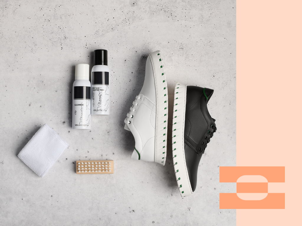 IAMBIC luxury shoe care kit for VIP customers, featuring leather cleaner, protector spray, brush, microfiber cloth, and MODEL T shoes in white and black arranged on a stone surface.