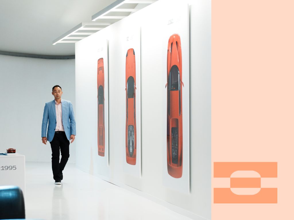 Ray Chang walking through a supercar design gallery wearing IAMBIC MODEL T precision-fit shoes, representing the intersection of luxury footwear, performance design, and AI-driven craftsmanship.